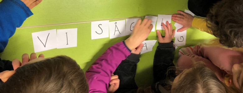 Barn skriver ord på golvet med bokstäver på lappar.
