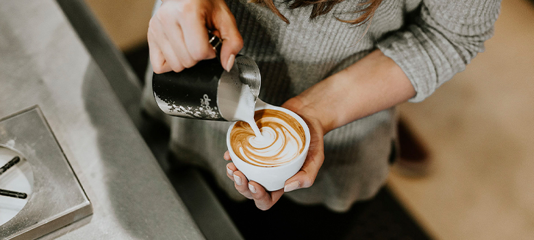 En person häller upp mjölk i en kaffekopp.