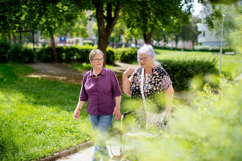 Två äldre människor går genom en park en solig dag