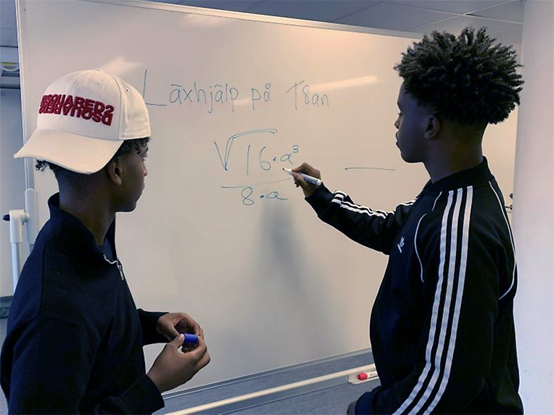 Två ungdomar som står vid en whiteboard och räknar matematik. 