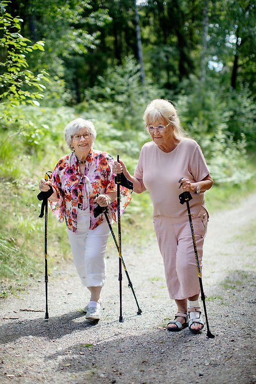 Två äldre damer som går på promenad med stavar utomhus.