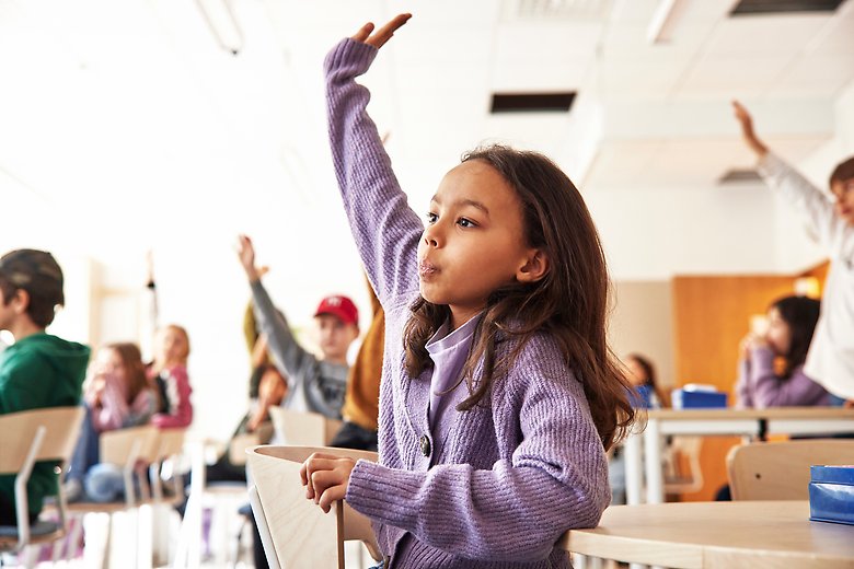 Flicka räcker upp handen i ett klassrum